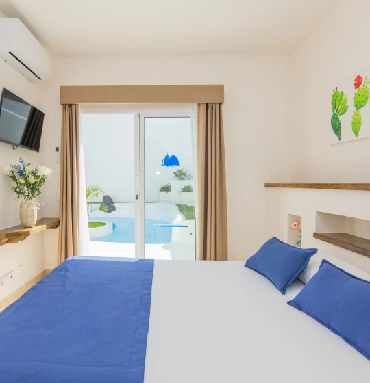 Habitaci&oacute;n luminosa con cama azul y vista a patio con piscina.
