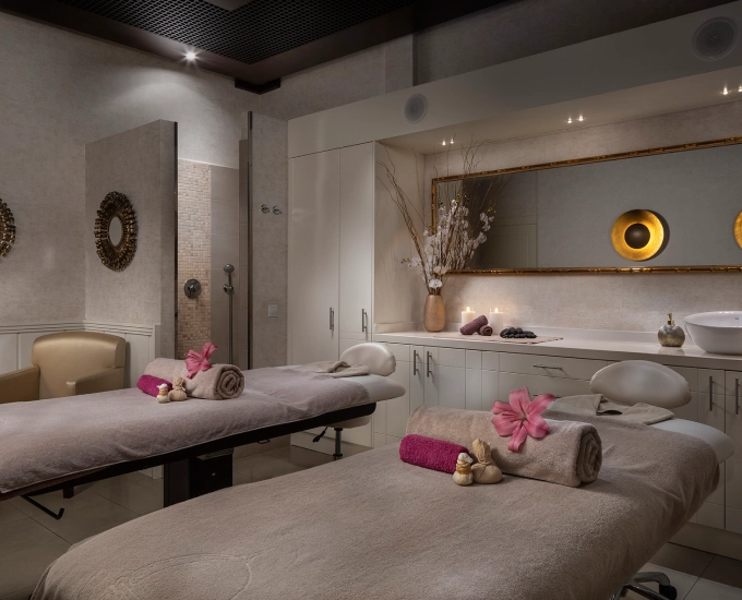 Sala de spa con dos camillas decoradas y espejo grande en la pared.