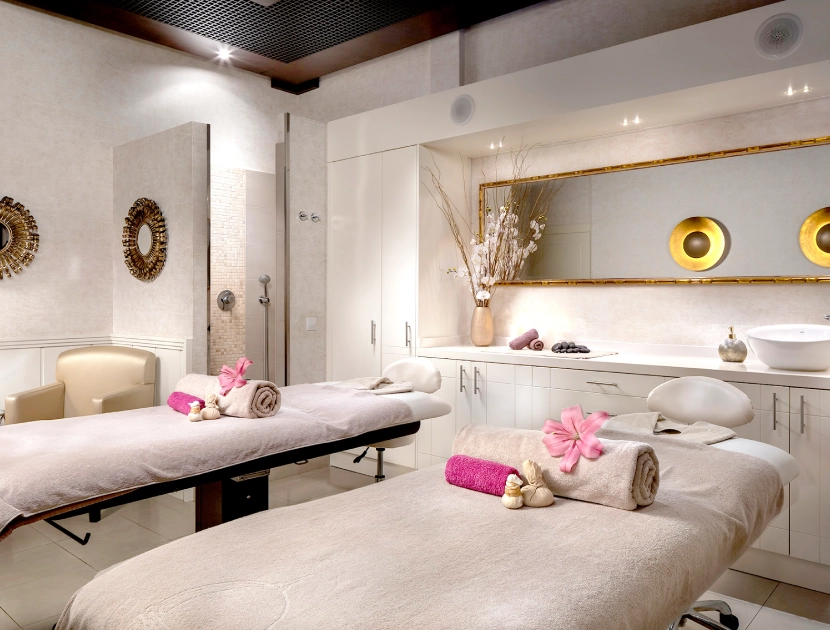 Sala de spa con dos camillas decoradas con toallas y flores rosas.