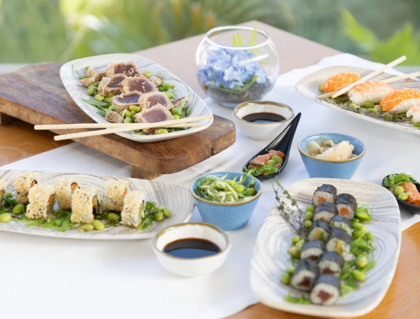 Platos de sushi variados en una mesa con cuencos y salsa de soja.