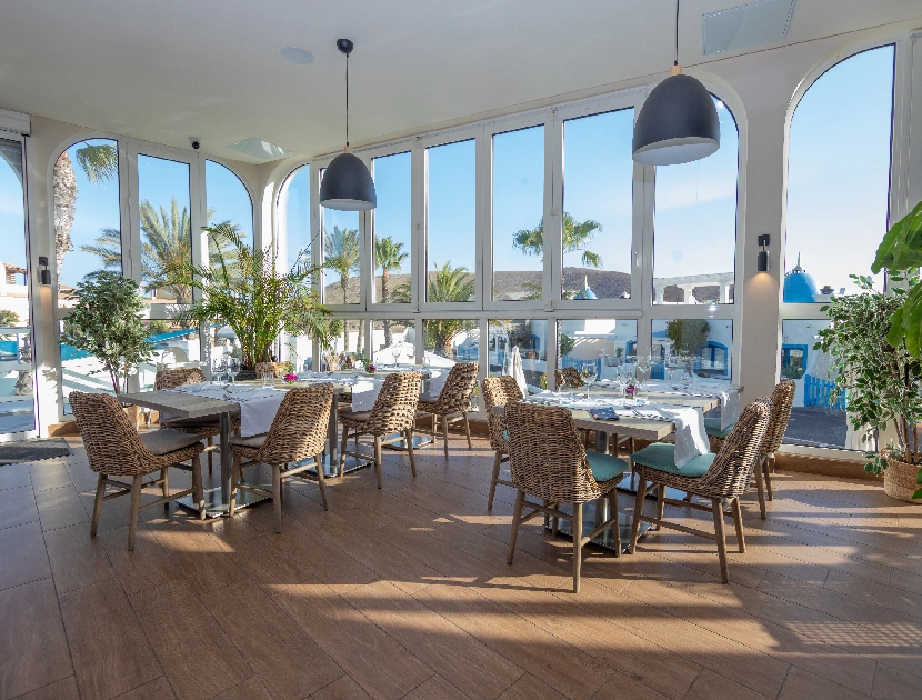 Restaurante luminoso con grandes ventanas y muebles de mimbre.