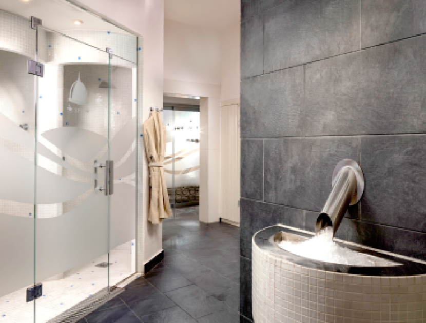 Spa moderno con ducha de vidrio y fuente de agua en la pared.