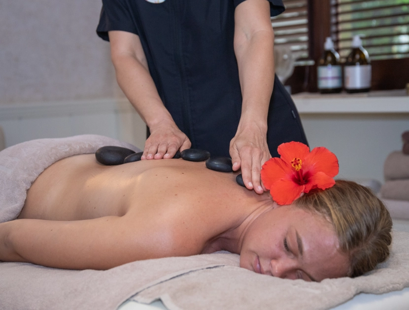 Mujer recibiendo masaje con piedras calientes, flor roja en el cabello.