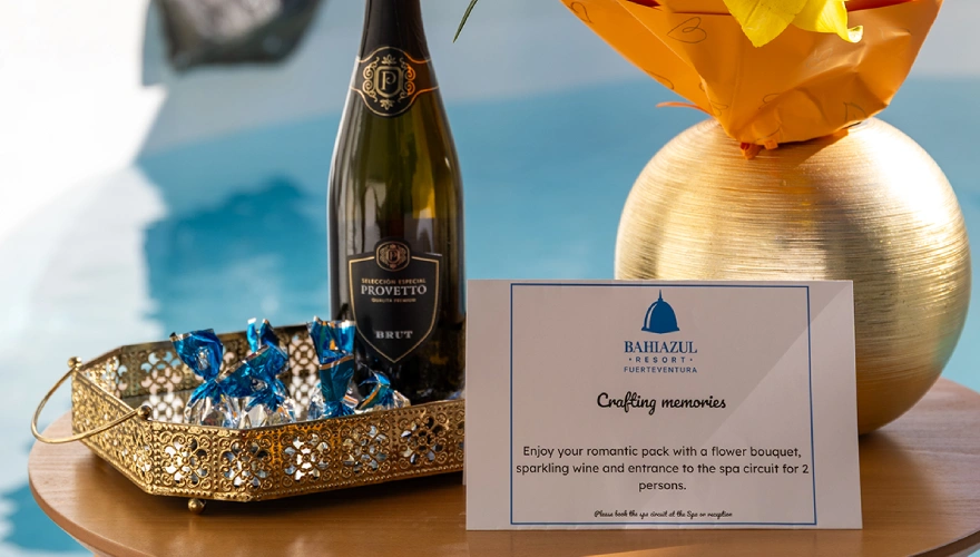 Botella de vino, dulces y tarjeta junto a una piscina.