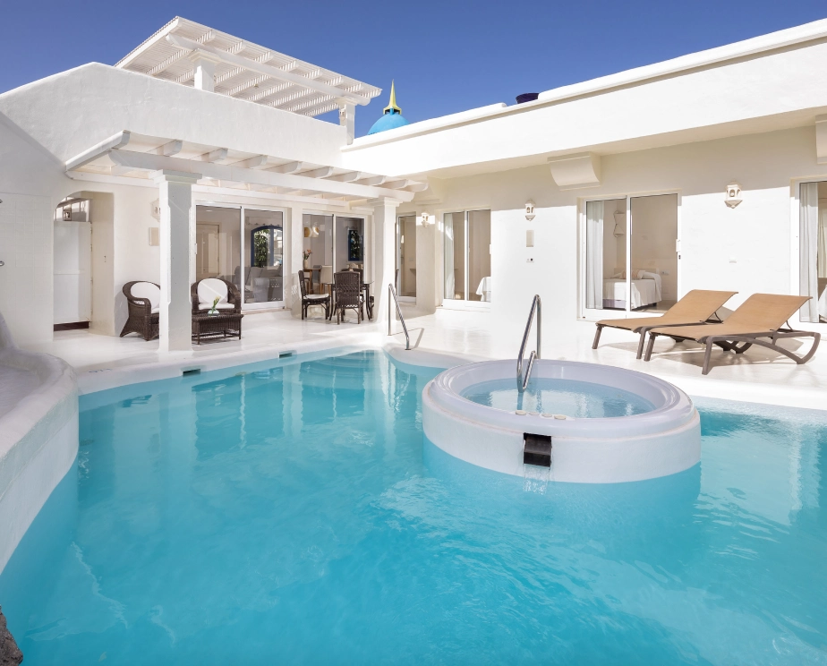 Casa blanca con piscina y jacuzzi, rodeada de sillas y mesas exteriores.