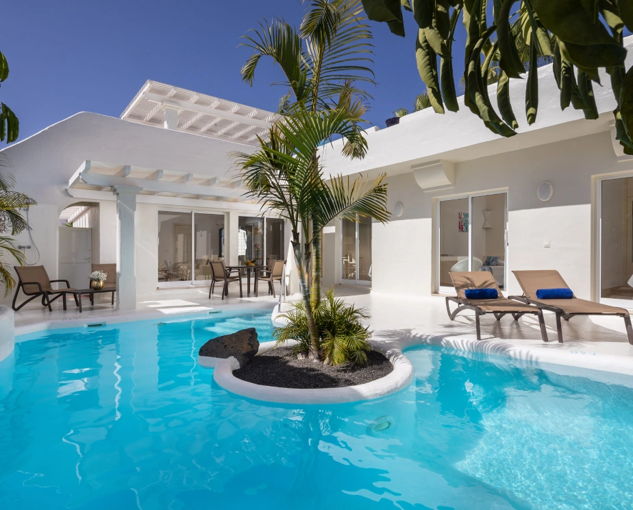 Piscina en un patio rodeado de tumbonas y plantas tropicales.