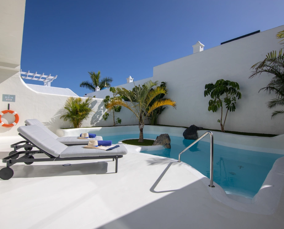 Piscina privada con tumbonas y plantas ex&oacute;ticas bajo un cielo despejado.