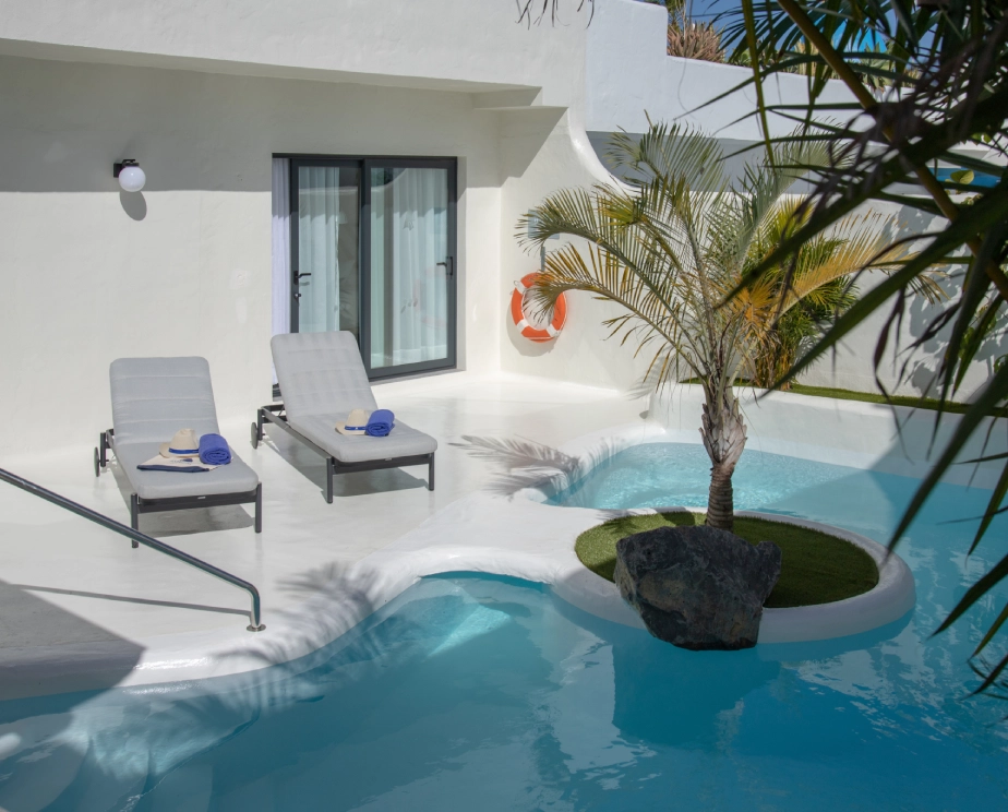 Piscina con dos tumbonas, palmera y ventanas corredizas en un entorno moderno.