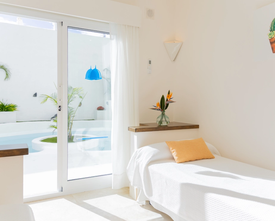 Habitaci&oacute;n minimalista con cama, jarr&oacute;n y vista a la piscina.