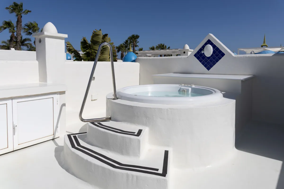 Jacuzzi blanco en una azotea soleada con escaleras y barandilla de metal.