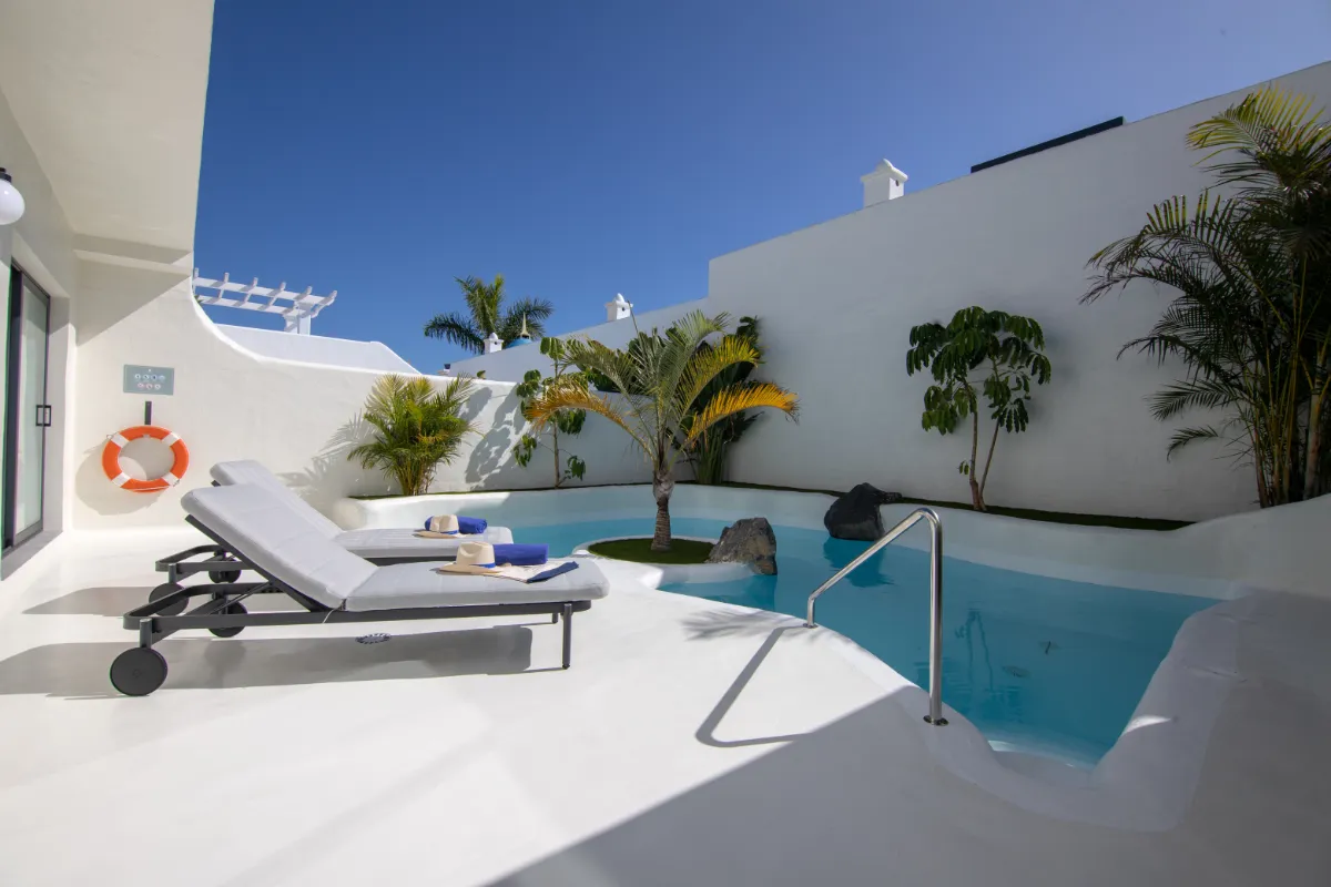 Terraza soleada con piscina y tumbonas, rodeada de plantas tropicales.