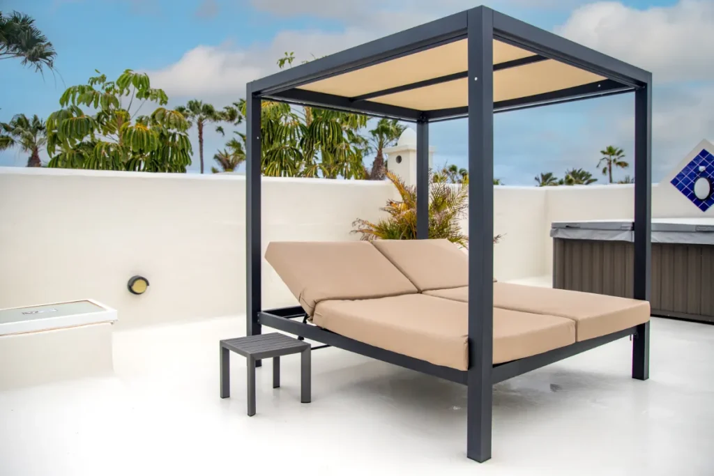 Cama balinesa doble con cojines beige bajo un toldo en una azotea.