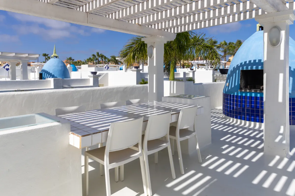 Terraza con muebles blancos y cúpulas azules, palmeras al fondo.