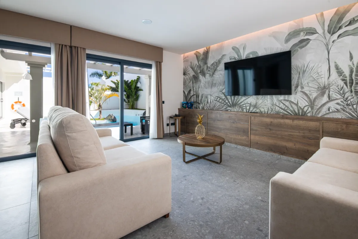 Sala moderna con sofá, mesa y TV, vista al patio con piscina.