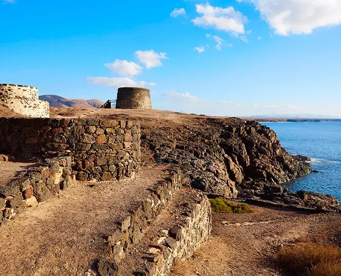 Ruinas de piedra en un acantilado junto al mar bajo un cielo azul.