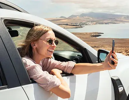 Persona sonriendo y tomando una foto desde un auto en un paisaje costero.
