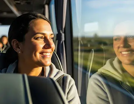 Mujer sonriente en un autob&uacute;s mirando el paisaje a trav&eacute;s de la ventana.