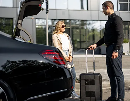 Persona junto a auto, con maleta y mujer conversando.