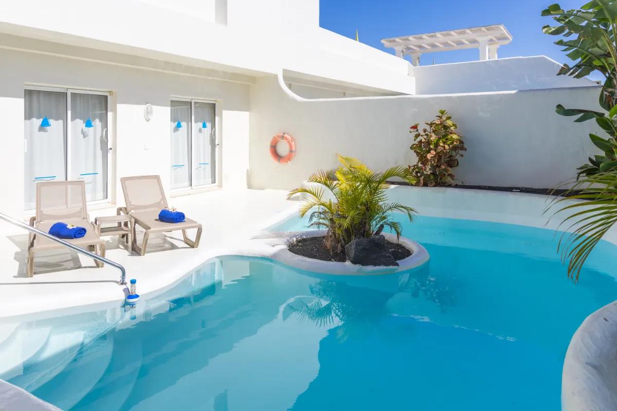 Piscina azul con tumbonas y toallas azules en un espacio exterior soleado.