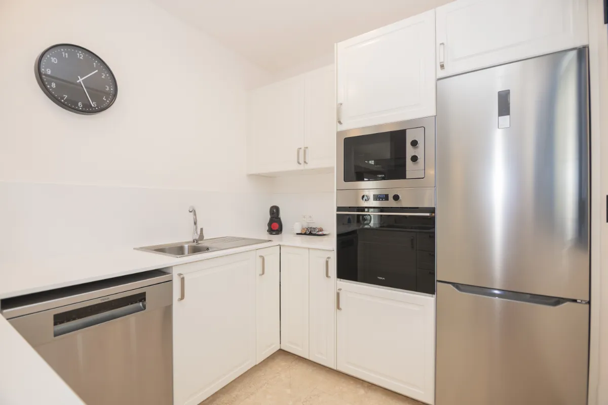 Cocina moderna blanca con electrodomésticos de acero inoxidable y un reloj en la pared.