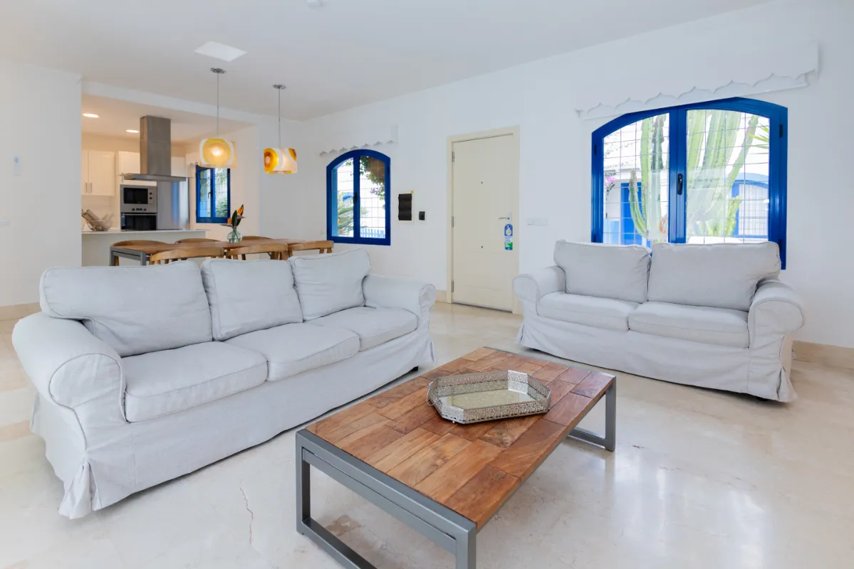 Sala moderna con sofás grises, mesa de madera y ventanas de marco azul.