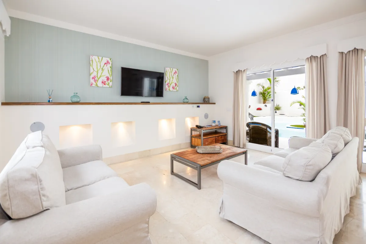 Sala luminosa con sofás blancos, mesa de madera y vista a piscina exterior.