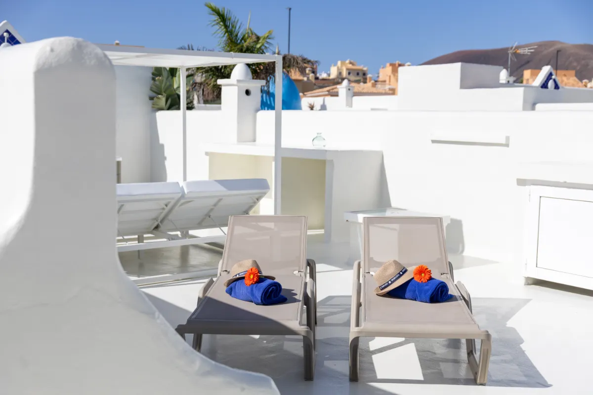 Dos camastros con sombreros y toallas azules sobre terraza blanca.