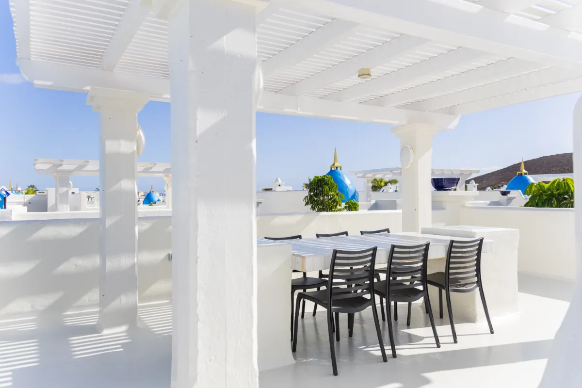 Terraza blanca con sillas negras y cielo despejado de fondo.