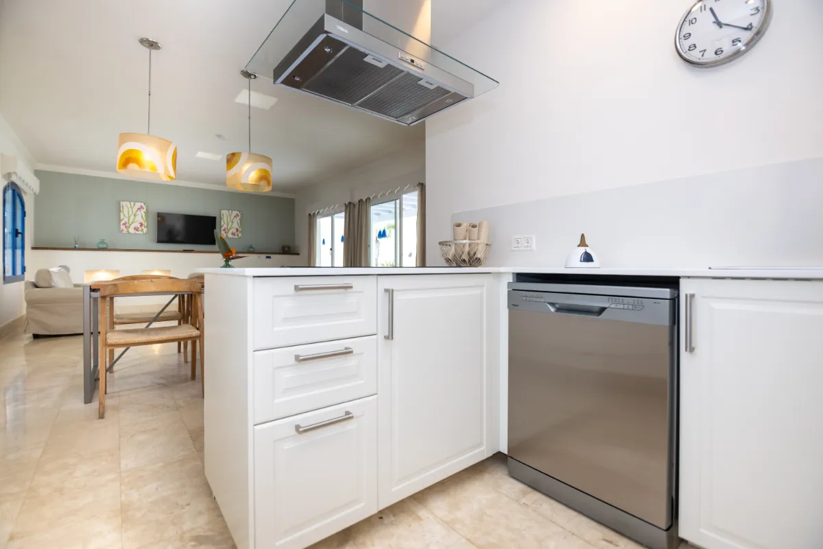 Cocina moderna con isla blanca, lámparas colgantes y reloj de pared.