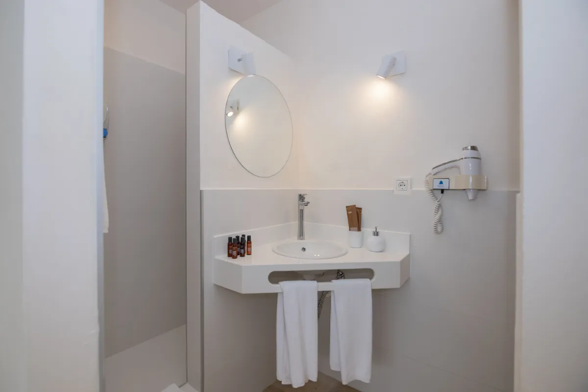 Baño moderno con lavabo, espejo, secador y amenities.