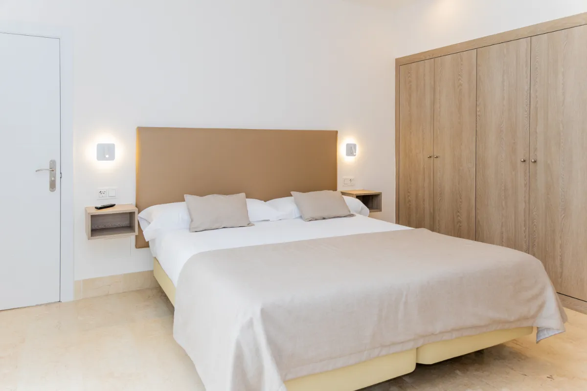 Cama doble en habitación moderna con armario y luz tenue.