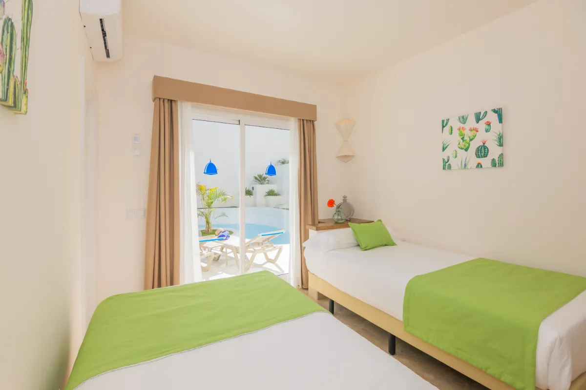 Dormitorio con dos camas, decoración verde y acceso a patio con piscina.