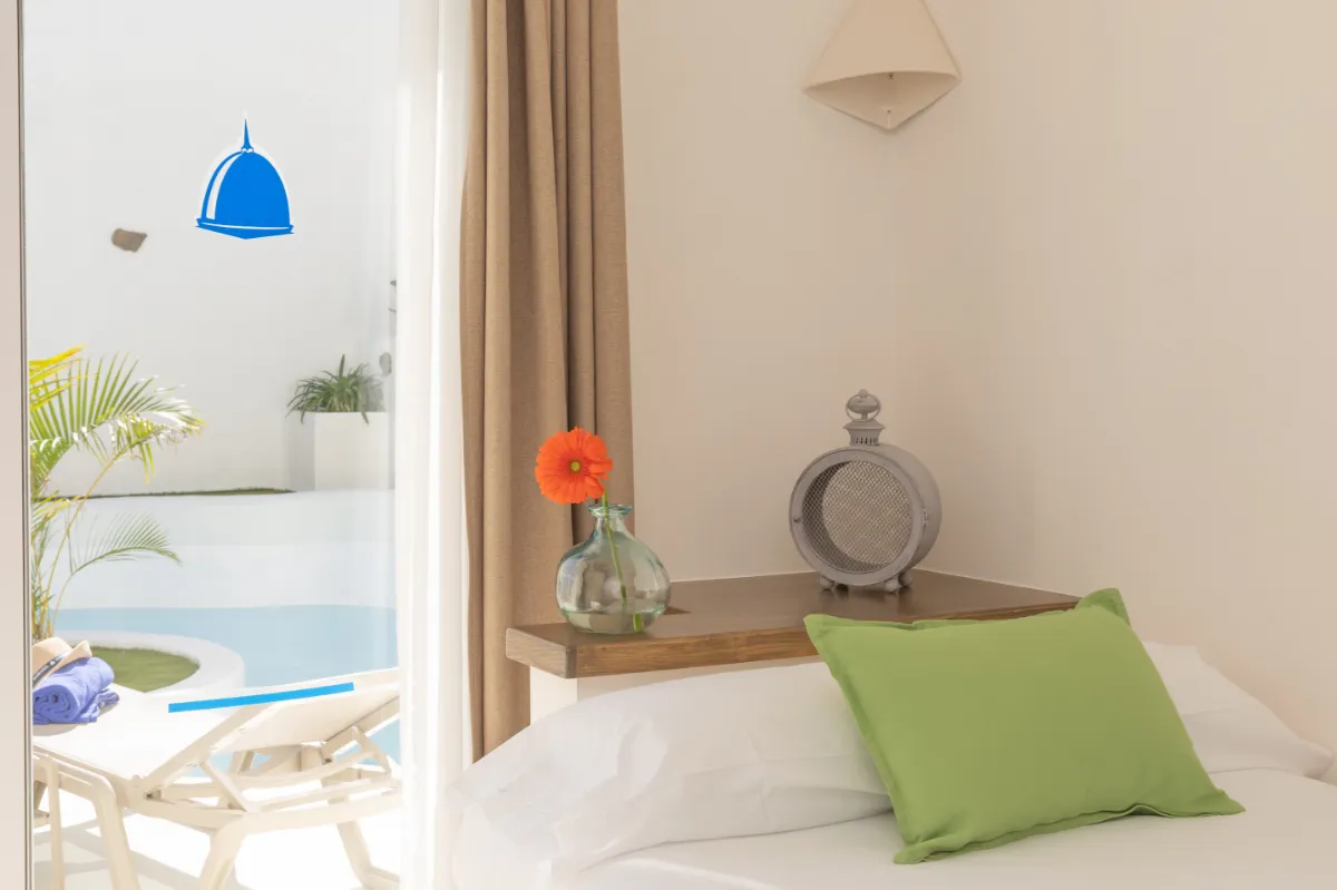 Habitación luminosa con cama, cojín verde y vista a la piscina.