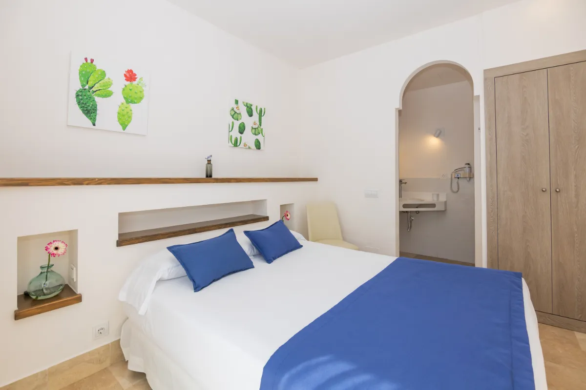 Habitación con cama, decoración de cactus, entrada a baño y armario de madera.