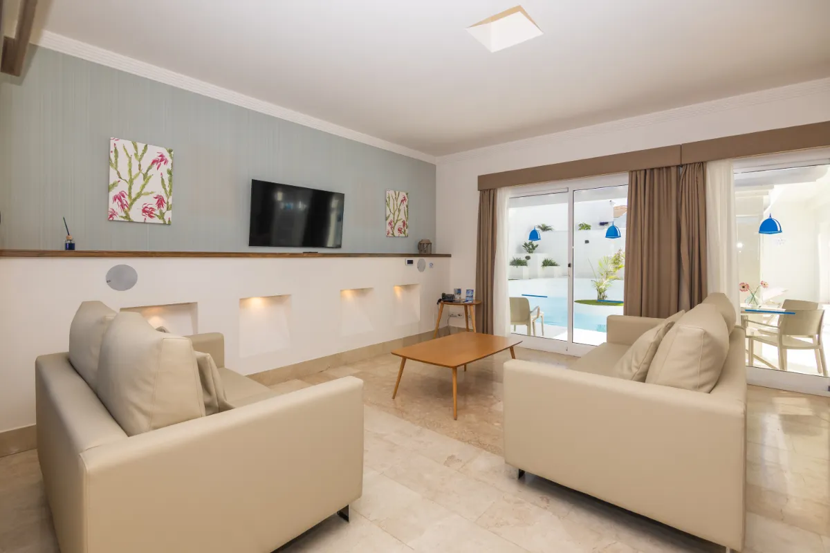 Sala moderna con sofás beige, TV y vista a la piscina.