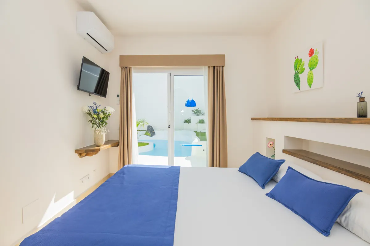 Dormitorio moderno con cama azul y vista a una piscina a través de una puerta.