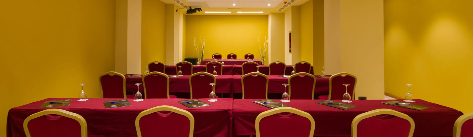 Sala de conferencias con sillas rojas y mesas cubiertas de manteles rojos.