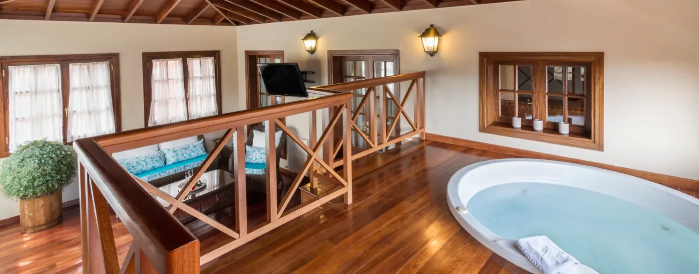 Sala interior con jacuzzi, sill&oacute;n, balc&oacute;n de madera y ventanas con cortinas.
