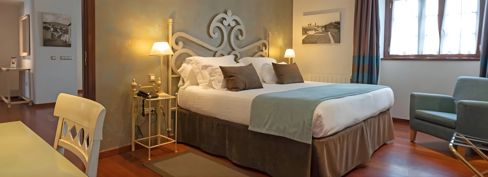 Habitaci&oacute;n de hotel con cama doble, l&aacute;mparas de noche y sill&oacute;n.