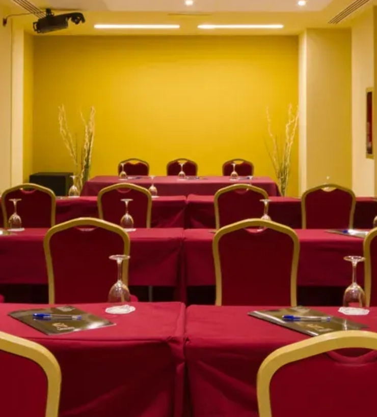 Sala de conferencias con sillas y mesas cubiertas de manteles rojos.