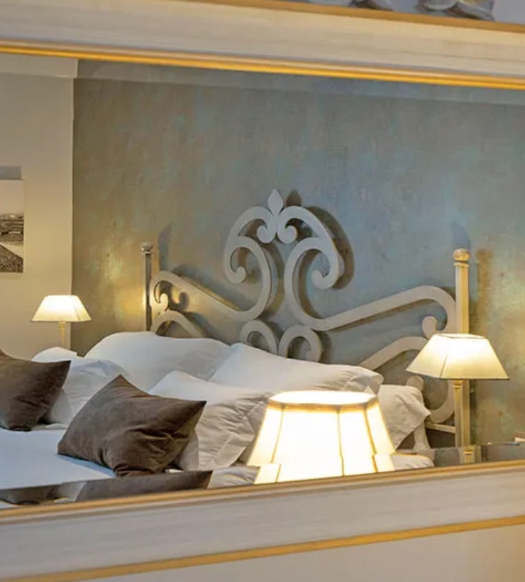 Habitaci&oacute;n elegante con cama, cojines y l&aacute;mparas de noche en un espejo.