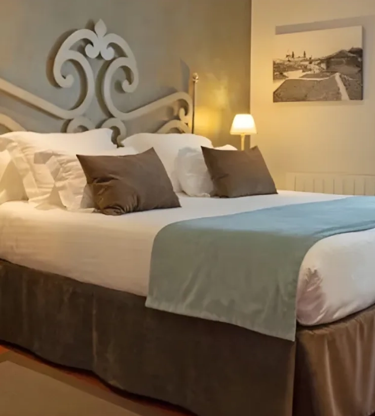 Cama con cabecero decorativo y l&aacute;mpara de mesa en habitaci&oacute;n acogedora.