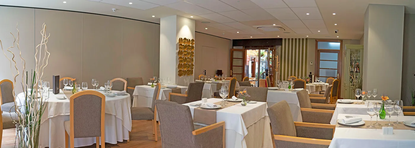 Restaurante elegante con mesas vestidas y sillas tapizadas.