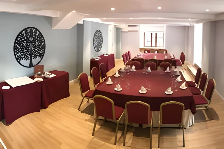 Sala con mesas redondas y sillas rojas, decorada con motivos de &aacute;rbol en la pared.