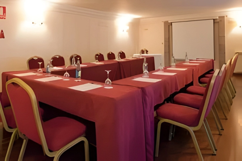 Sala de reuniones con mesa en forma de U y sillas rojas.