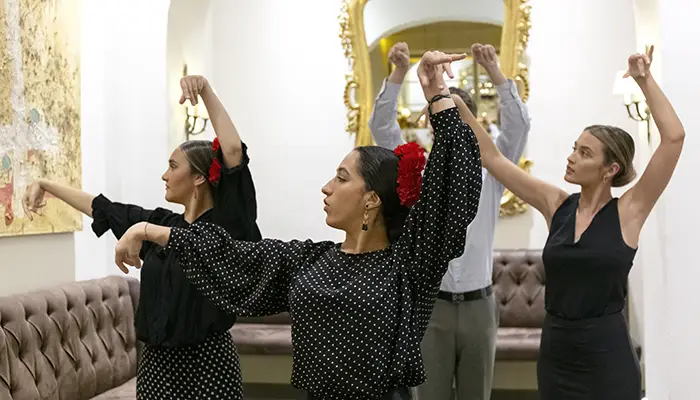 Personas practicando pasos de baile flamenco en un sal&oacute;n con espejos.