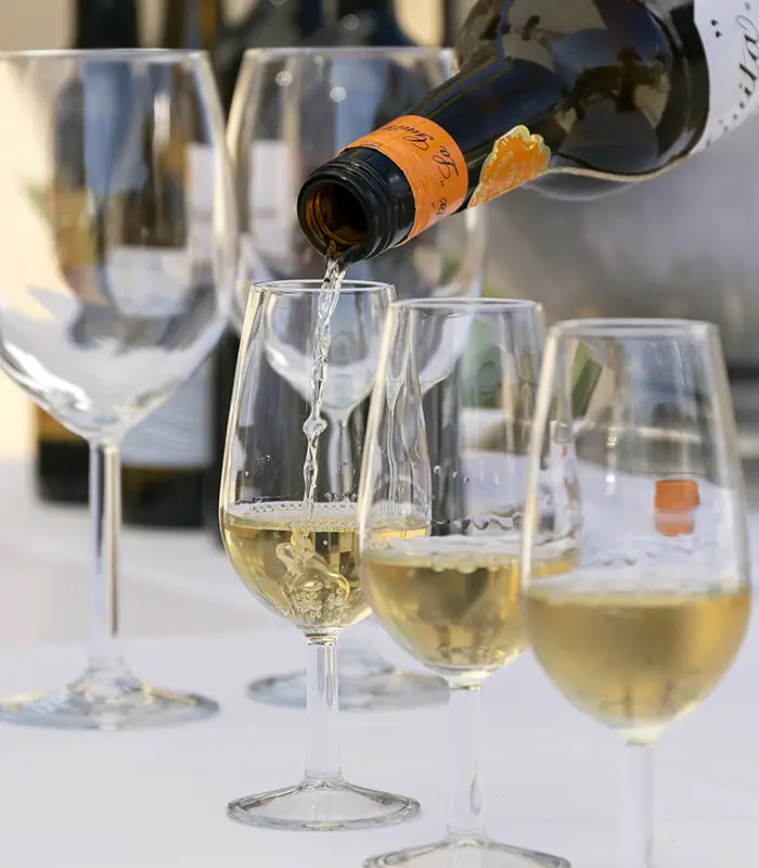 Vino blanco siendo servido en copas sobre una mesa blanca.