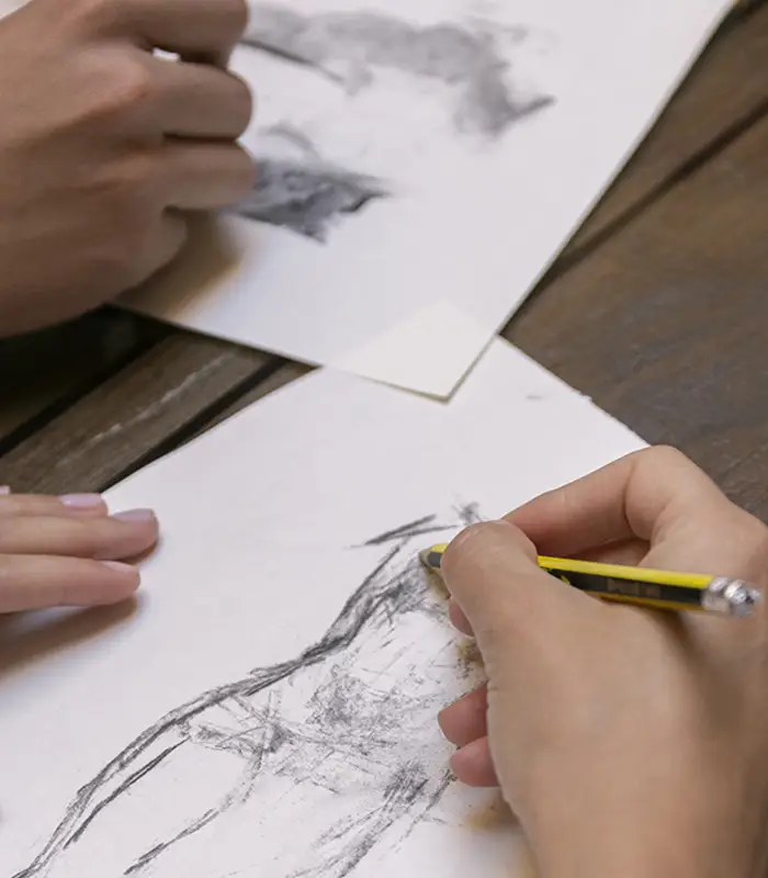 Manos dibujando bocetos en papel con l&aacute;piz sobre una mesa de madera.
