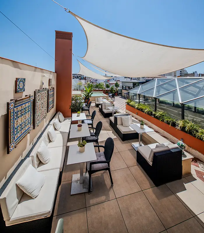 Terraza con muebles de exterior, mesas, sillas y decoraci&oacute;n en un d&iacute;a soleado.