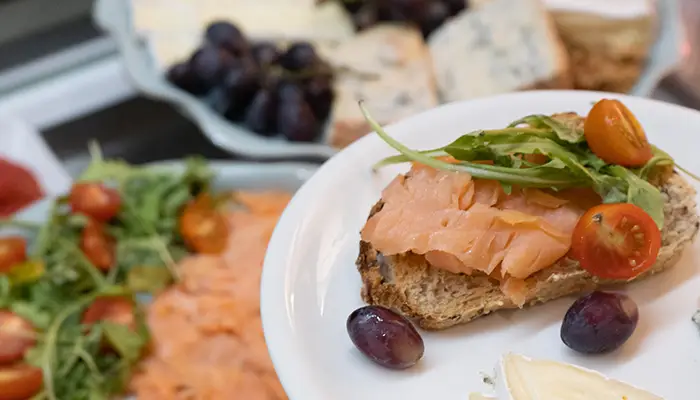 Tostada con salm&oacute;n, r&uacute;cula y tomate; uvas y queso alrededor.